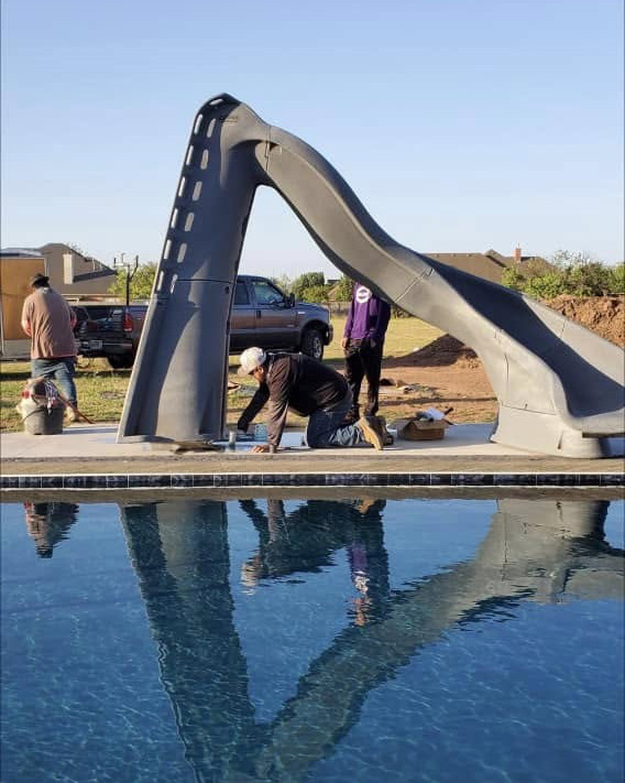 Crew installing a pool slide beside finished dark-tile pool