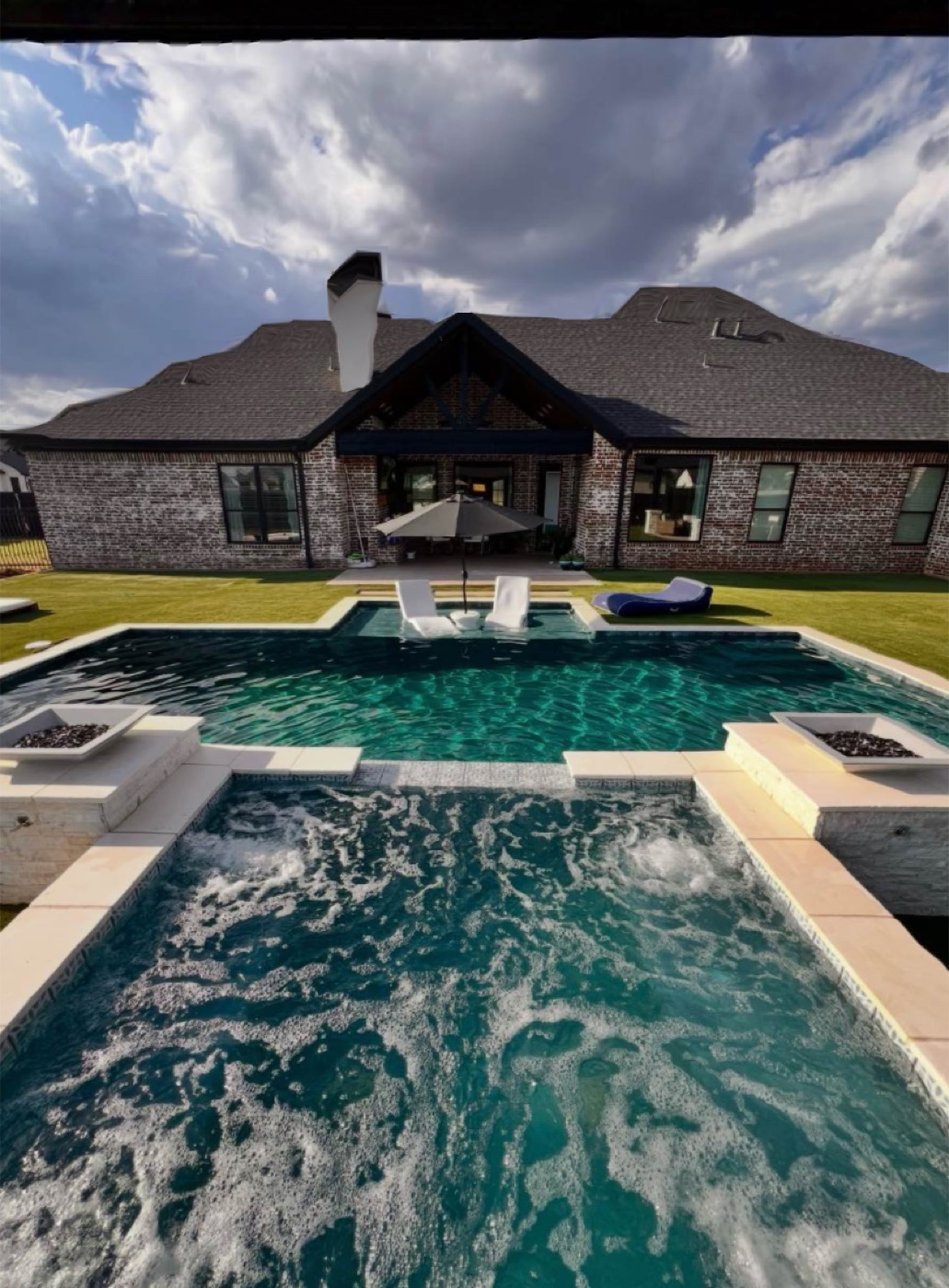 Completed pool and elevated spa with twin fire bowls behind a brick home