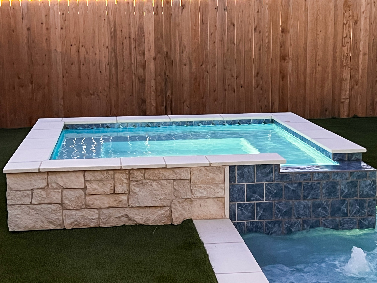 Raised spa with stacked stone and blue glass tile glowing at dusk