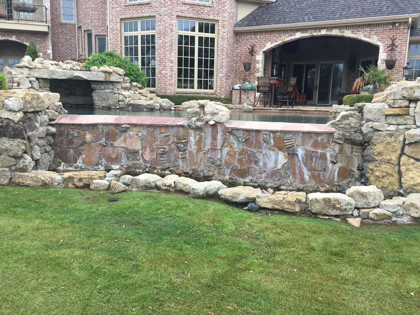 Natural stone waterfall wall and grotto beside a brick home
