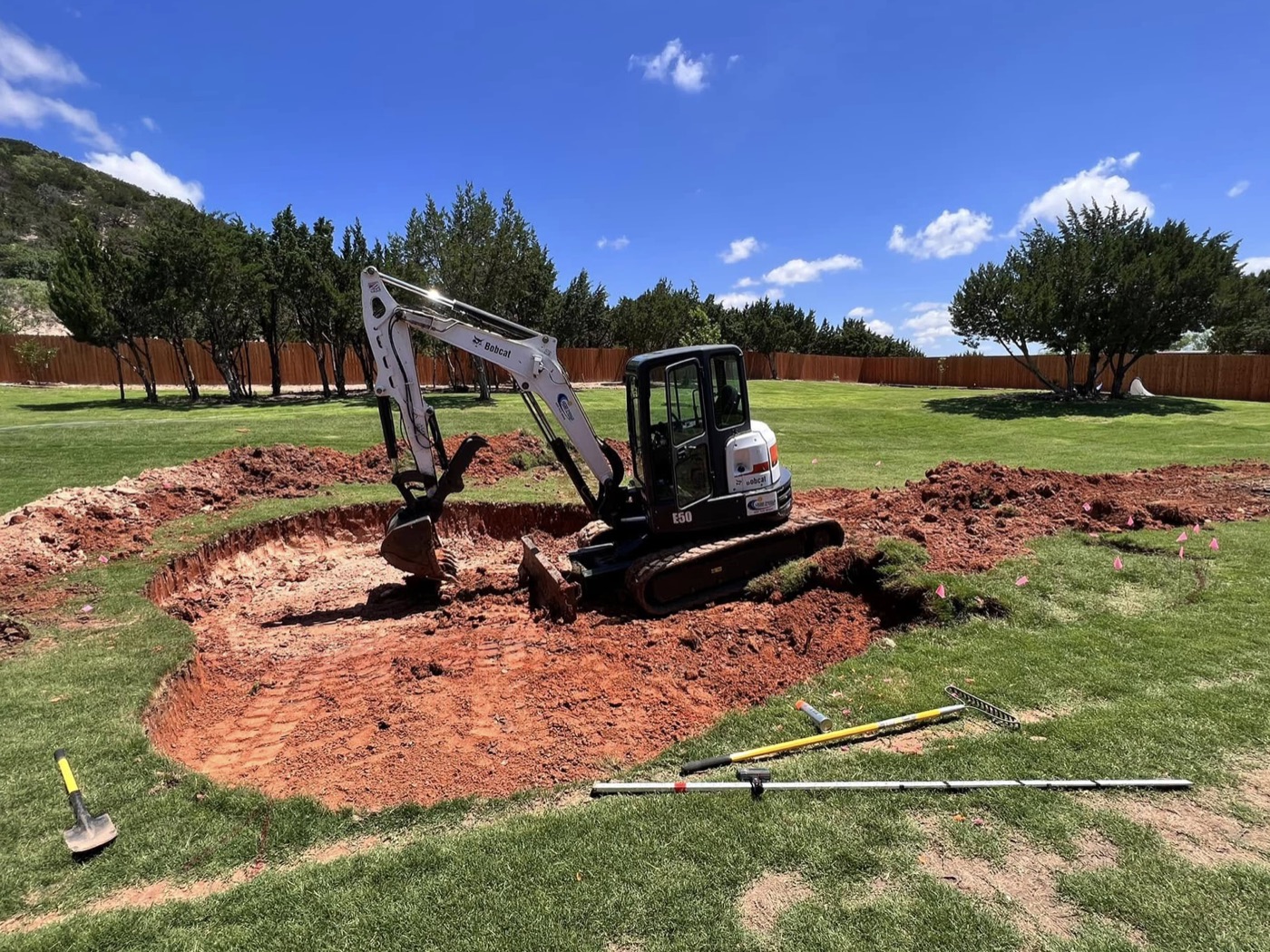 Excavator digging a new freeform pool in a green backyard