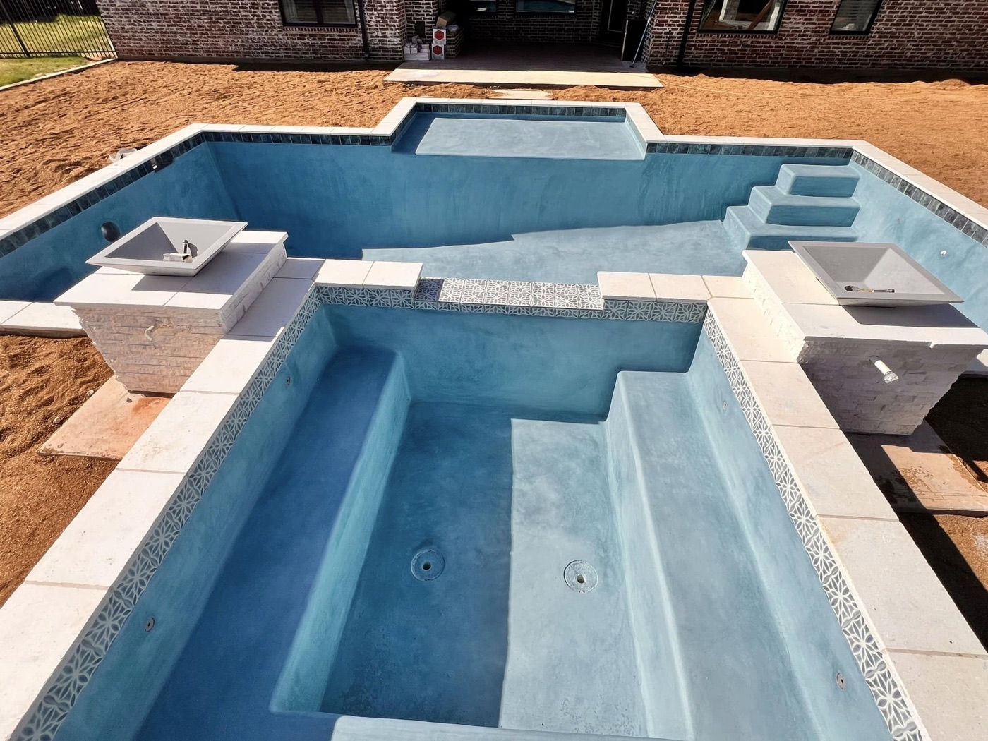 Geometric pool and spa with stacked-stone fire bowl pedestals during plaster stage